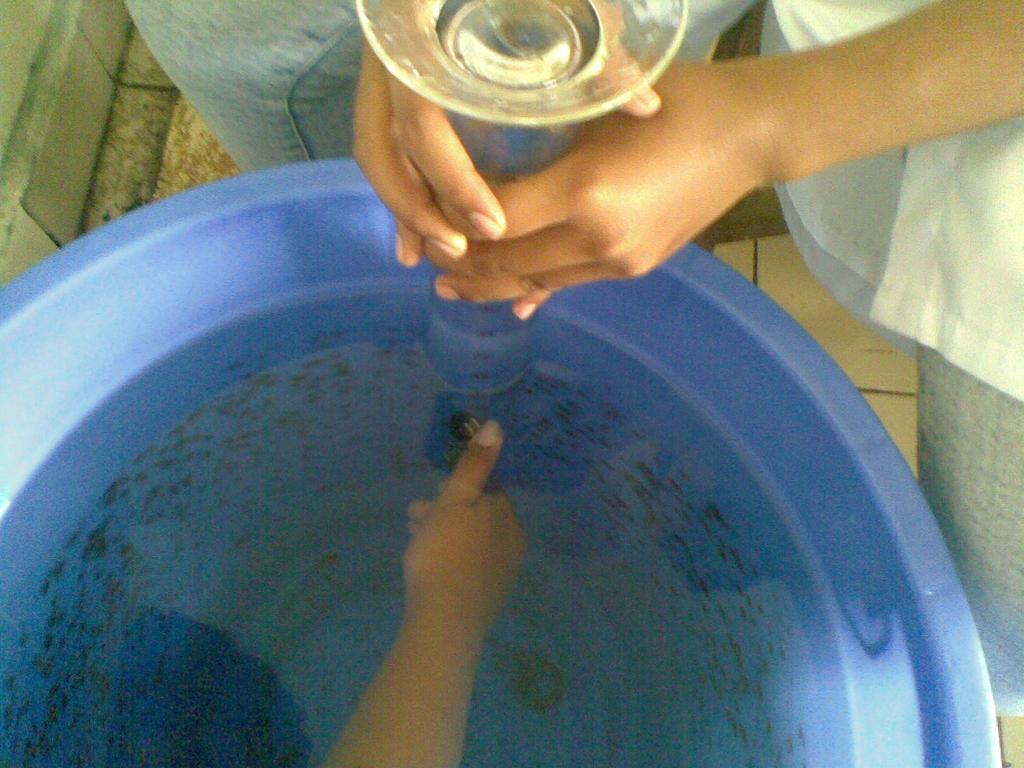 Gelas ukur yang berisi penuh air terbalik diletakkan diatas ember yang berisi air.