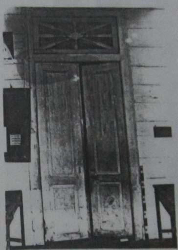 Daun pintu dibuat dari kayu berwarna hijau, terdiri dari dua daun pintu dan